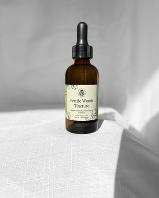 fertile womb herbal tincture by the fertile glow in a 2 ounce amber dropper bottle on a white background. Label says fertile womb herbal supplement supports fertility and hormone balance. Tan and green label with black flowers.